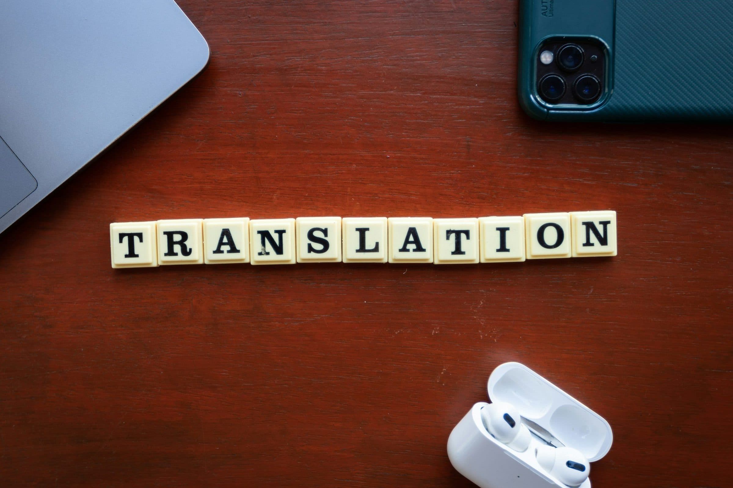 Ein Smartphone und kabellose Ohrhörer neben Buchstabensteinen mit dem Wort TRANSLATION